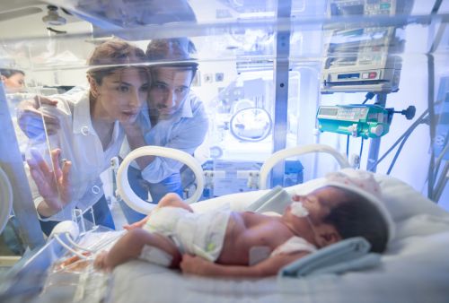 Worried young couple looking at their premature newborn in an incubator with oxygen at neonatal intensive care unit.